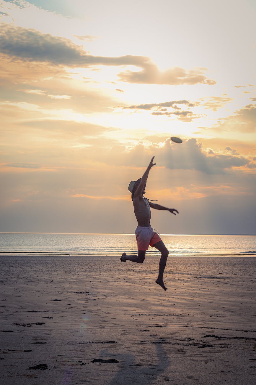 A man jumps in the air to catch a frisbee at sunset on a beach.
