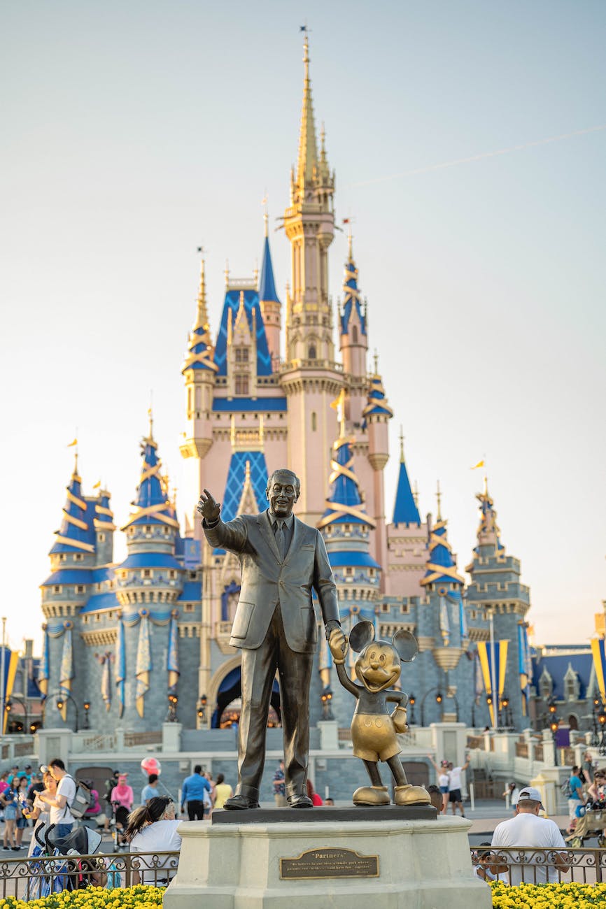 A statue of Walt Disney holding Mickey Mouse's hand stands in front of Cinderella's Castle at Walt Disney World in Orlando Florida.