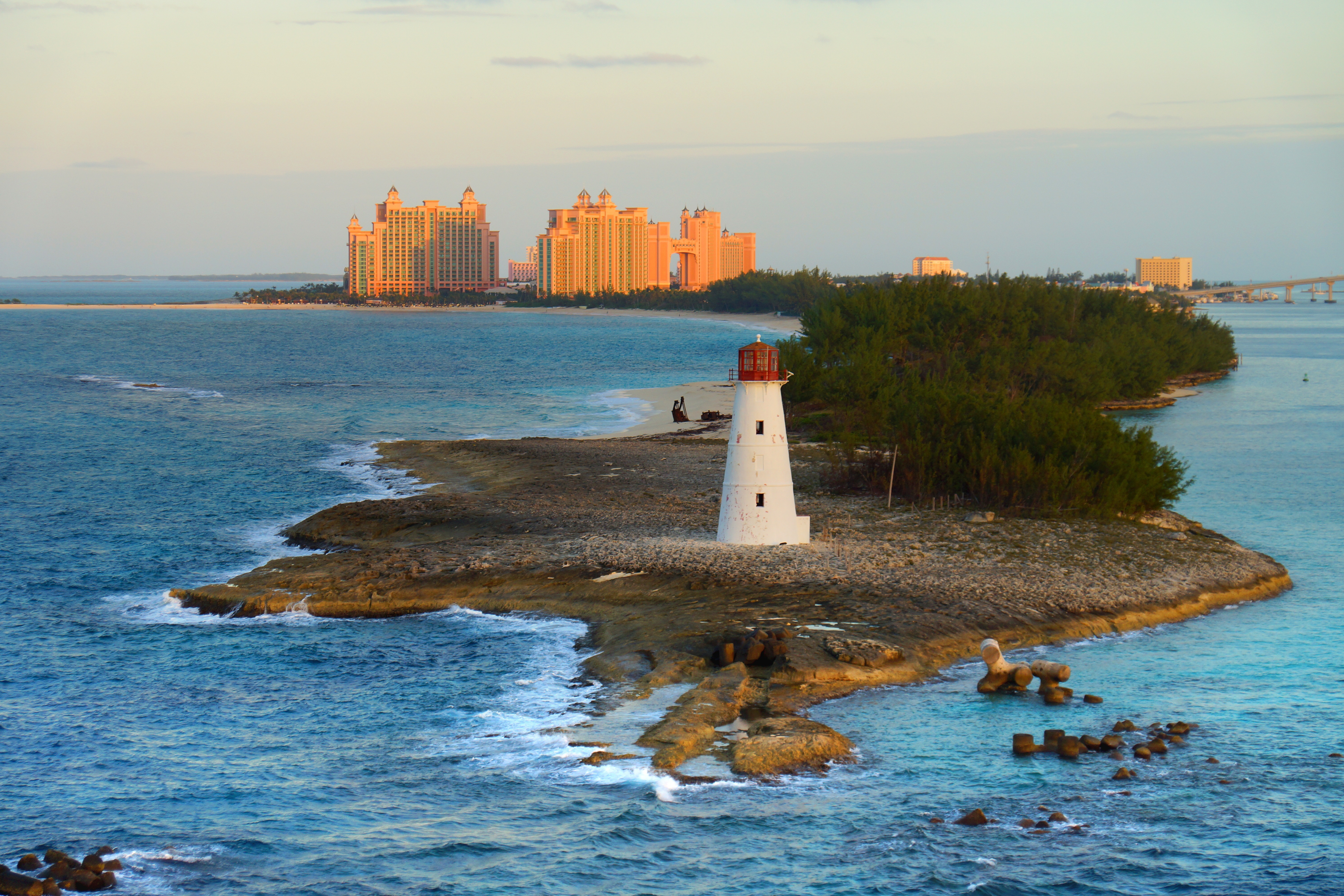 Waves crash upon Paradise Island in the Bahamas, with Nassau Harbour Lighthouse in the foreground and the large pink buildings of Atlantis Resort in the background.